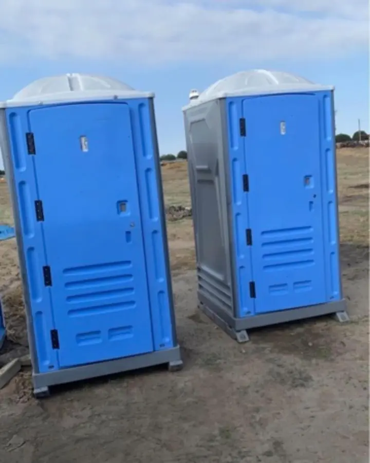 Two blue standard porta potties on a dirt jobsite